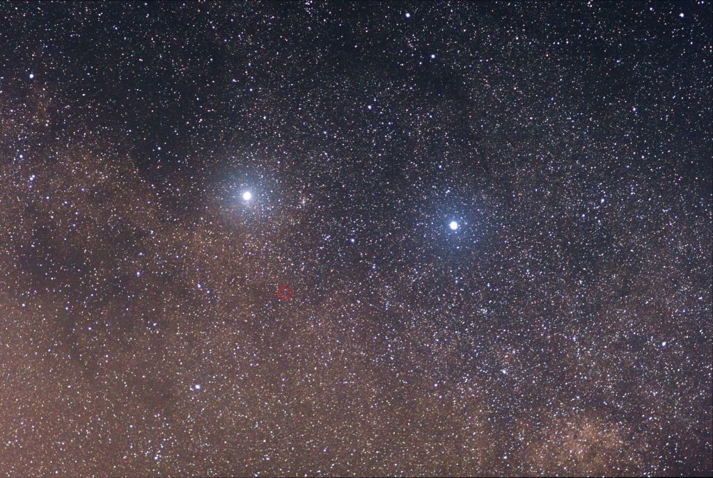 The two bright stars are (left) Alpha Centauri and (right) Beta Centauri. The faint red star in the center of the red circle is Proxima Centauri. Taken with Canon 85mm f/1.8 lens with 11 frames stacked, each frame exposed 30 seconds. Image Credit: Skatebiker / Wikimedia Commons.