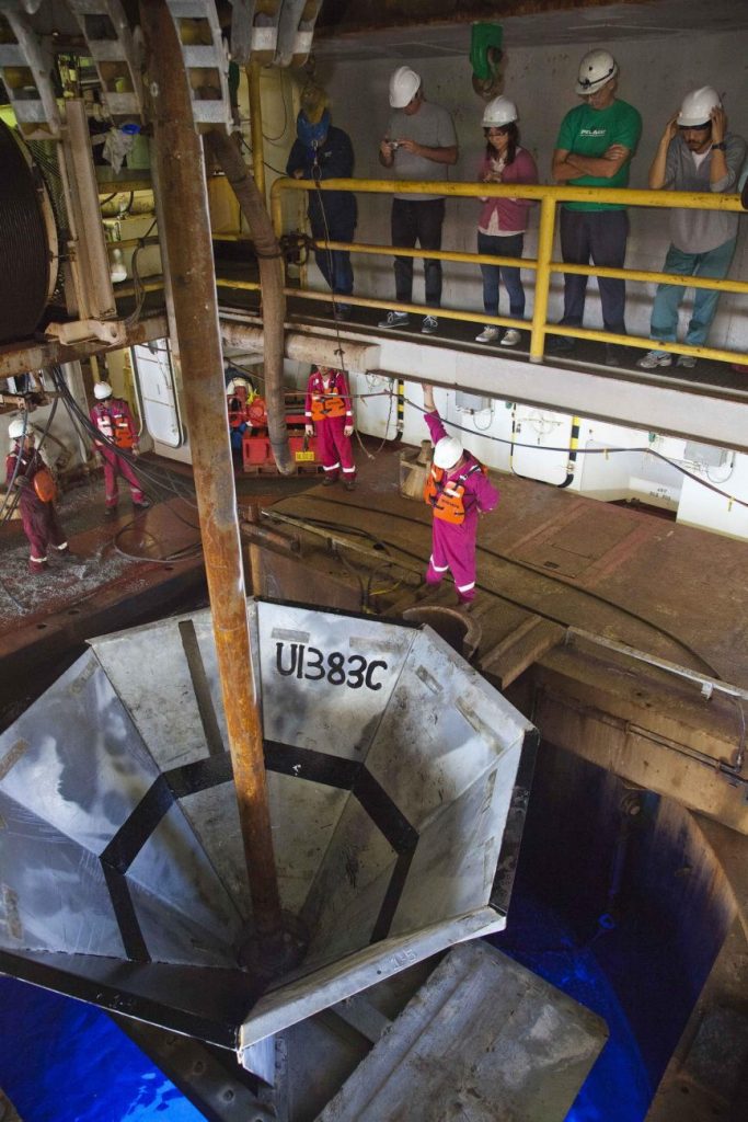 The re-entry cone is welded together around the drill pipe, then lowered down the pipe to guide reinsertion before changing drill bits. IODP, CC BY-ND 4.0.