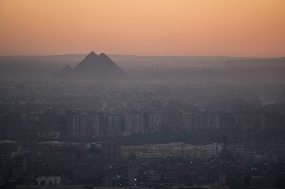 The pyramids of Giza in the background, surrounded by a jungle of modern buildings. Shutterstock.