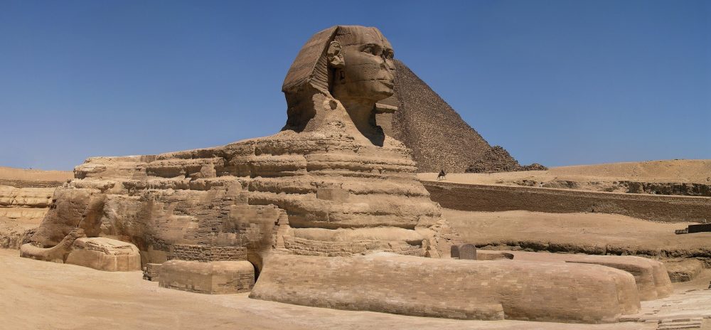 A wide panoramic view of the Great Sphinx with Great Pyramid of Khufu in background. Shutterstock.