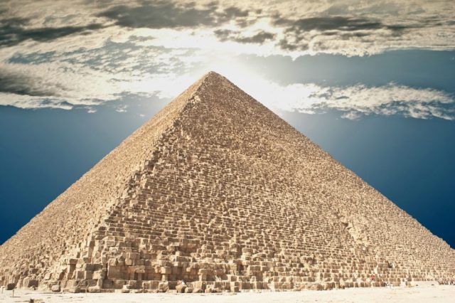 The Great Pyramid of Giza and people climbing its supermassvie stones. Shutterstock.