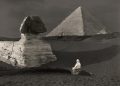 A view of the Sphinx still covered in sand. Behind it, the Great Pyramid.