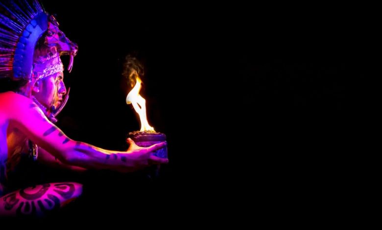 An image showing a man wearing a Maya costume holding a bowl lit on fire. Jumpstory.