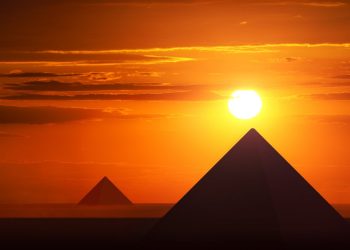 An image of the Egyptian pyramids at Giza and the sun just above them. Shutterstock.