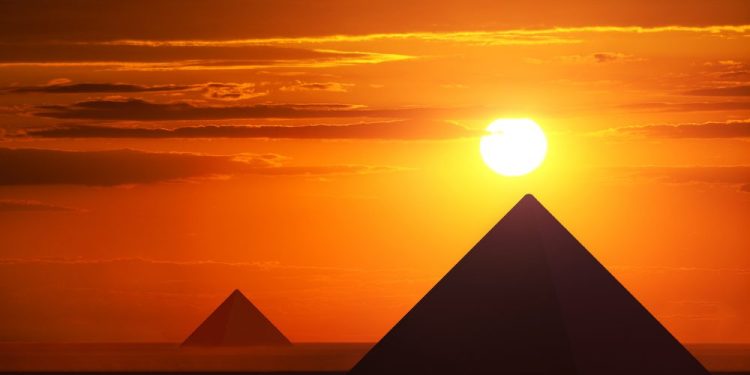 An image of the Egyptian pyramids at Giza and the sun just above them. Shutterstock.