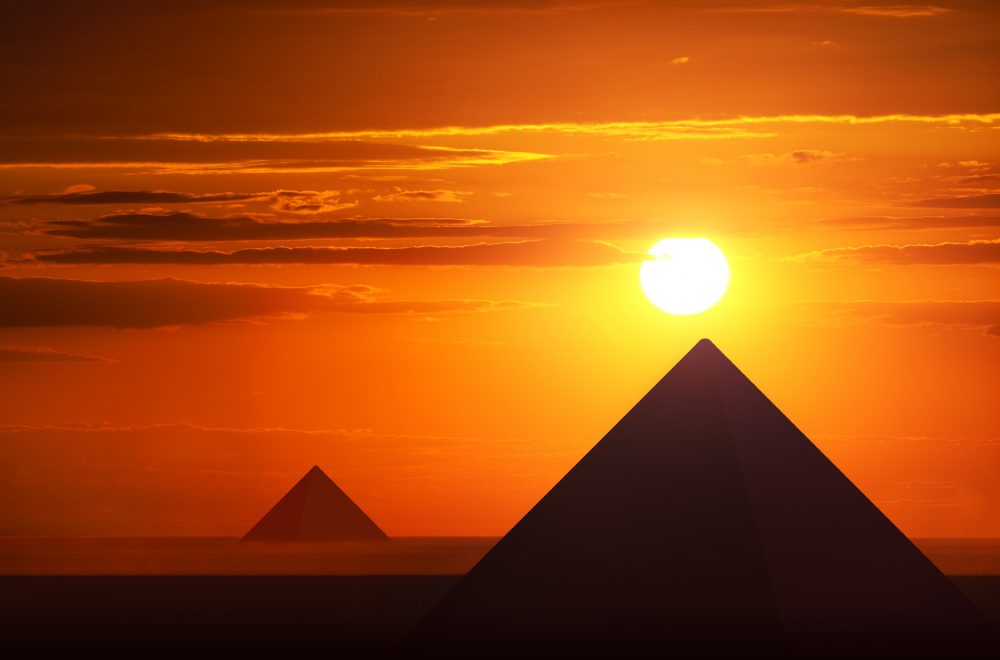 An image of the Egyptian pyramids at Giza and the sun just above them. Shutterstock.
