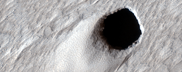 This image taken by the HiRISE camera aboard the MRO shows a massive lava tube leading towards the interior of Mars. Image Credit: NASA/JPL/UArizona.
