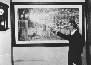 Nikola Tesla standing in front of one of his most famous photographs.