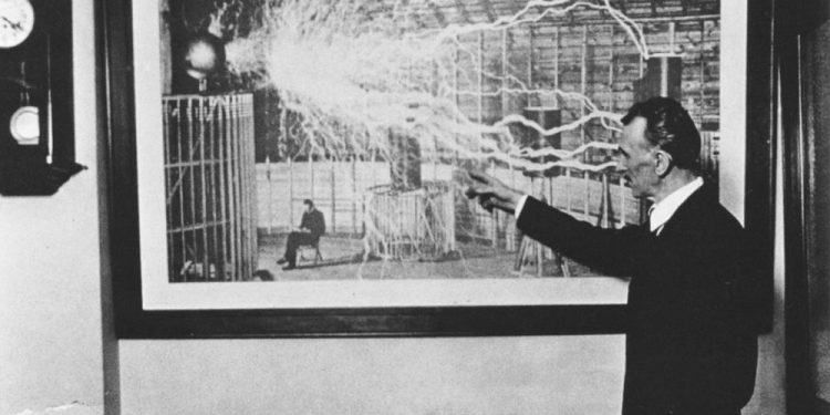 Nikola Tesla standing in front of one of his most famous photographs.