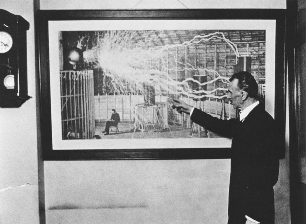 Nikola Tesla standing in front of one of his most famous photographs.