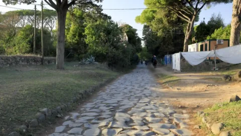 Worn stone paving along the Appian Way near Rome, with trees lining the road.