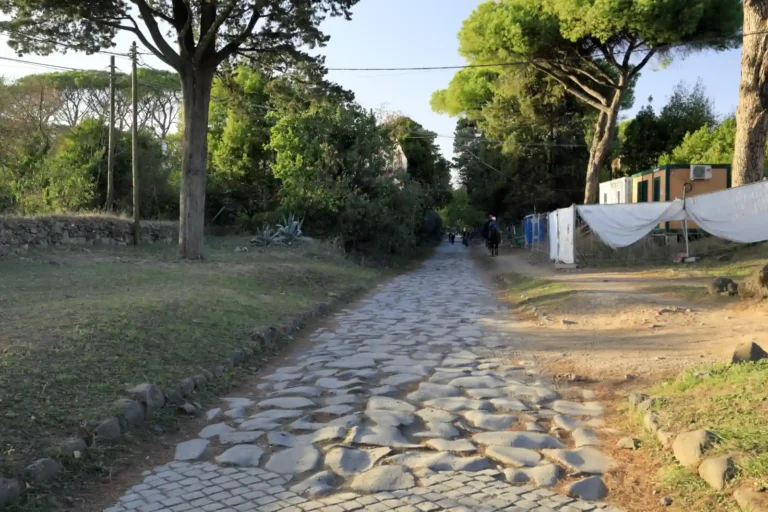 Worn stone paving along the Appian Way near Rome, with trees lining the road.