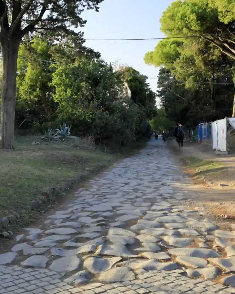 Worn stone paving along the Appian Way near Rome, with trees lining the road.