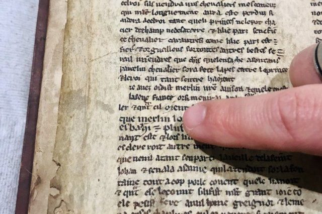 A researcher points to the name of Merlin in the 13th century manuscript. Credit: University of Bristol