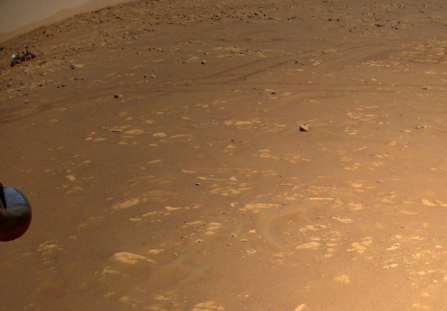 An image captured by the Ingenuity Mars Helicopter on April 25, 2021. On the left, you can see the Perseverance rover and and in the middle - its tracks on the surface. Credit: NASA/JPL-Caltech