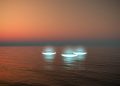 An illustration showing three UFOs hovering above the ocean. Depositphotos.