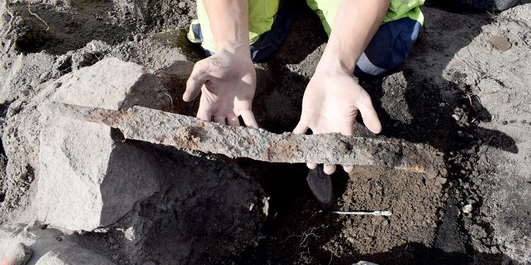 A photograph of an archaeologist holding one of the swords. Image Credit: arkeologerna.