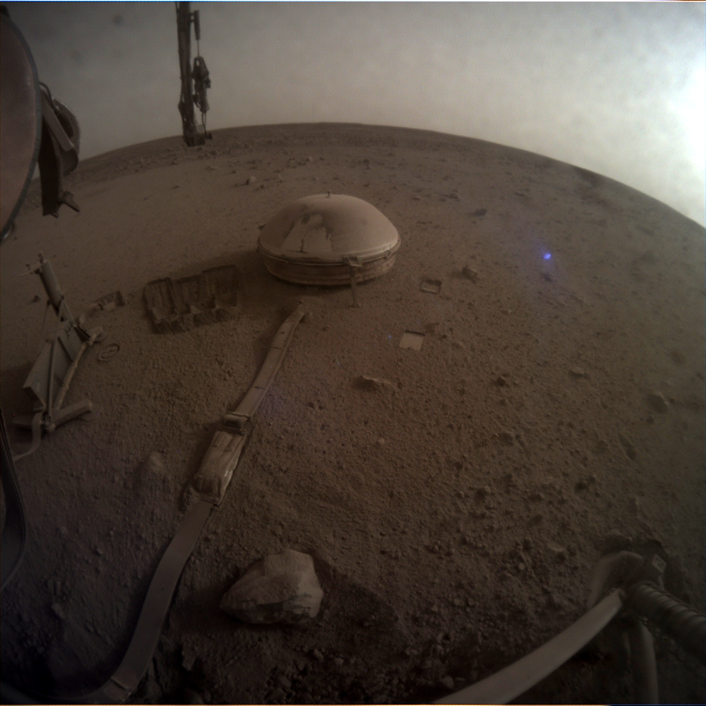 Another photograph snapped by InSight showing parts of its dust-covered Seismograph. Image Credit: NASA.