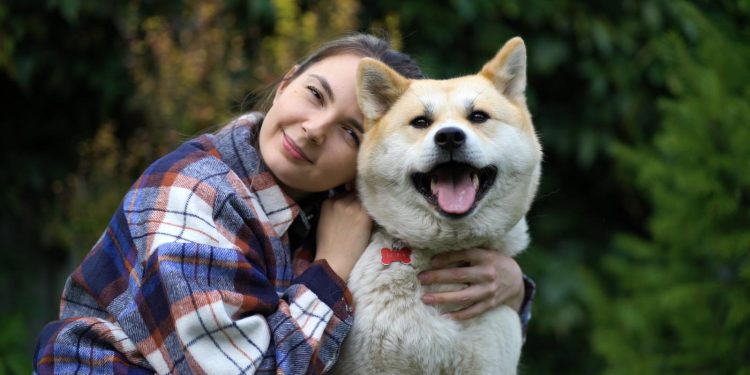 The girl hugs the dog and puts her head on her and look at the camera.