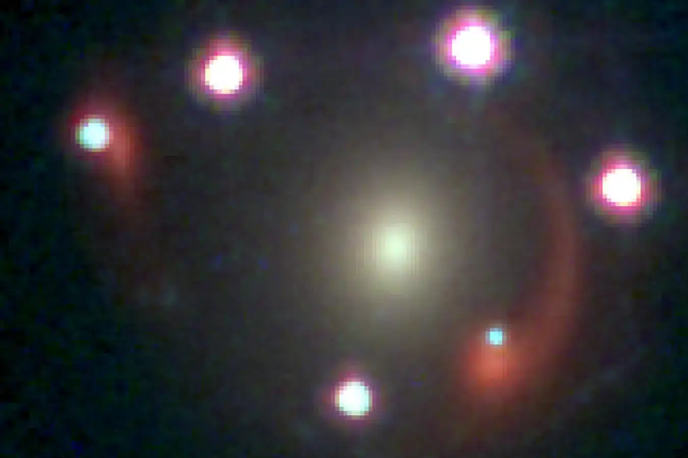 Six distinct images of the same quasar are visible as white or bluish spots, resulting from the gravitational lensing effect caused by two galaxies. One of these galaxies appears as a bright patch at the center, while the other forms a red arc. Credit: F. Dux et al.