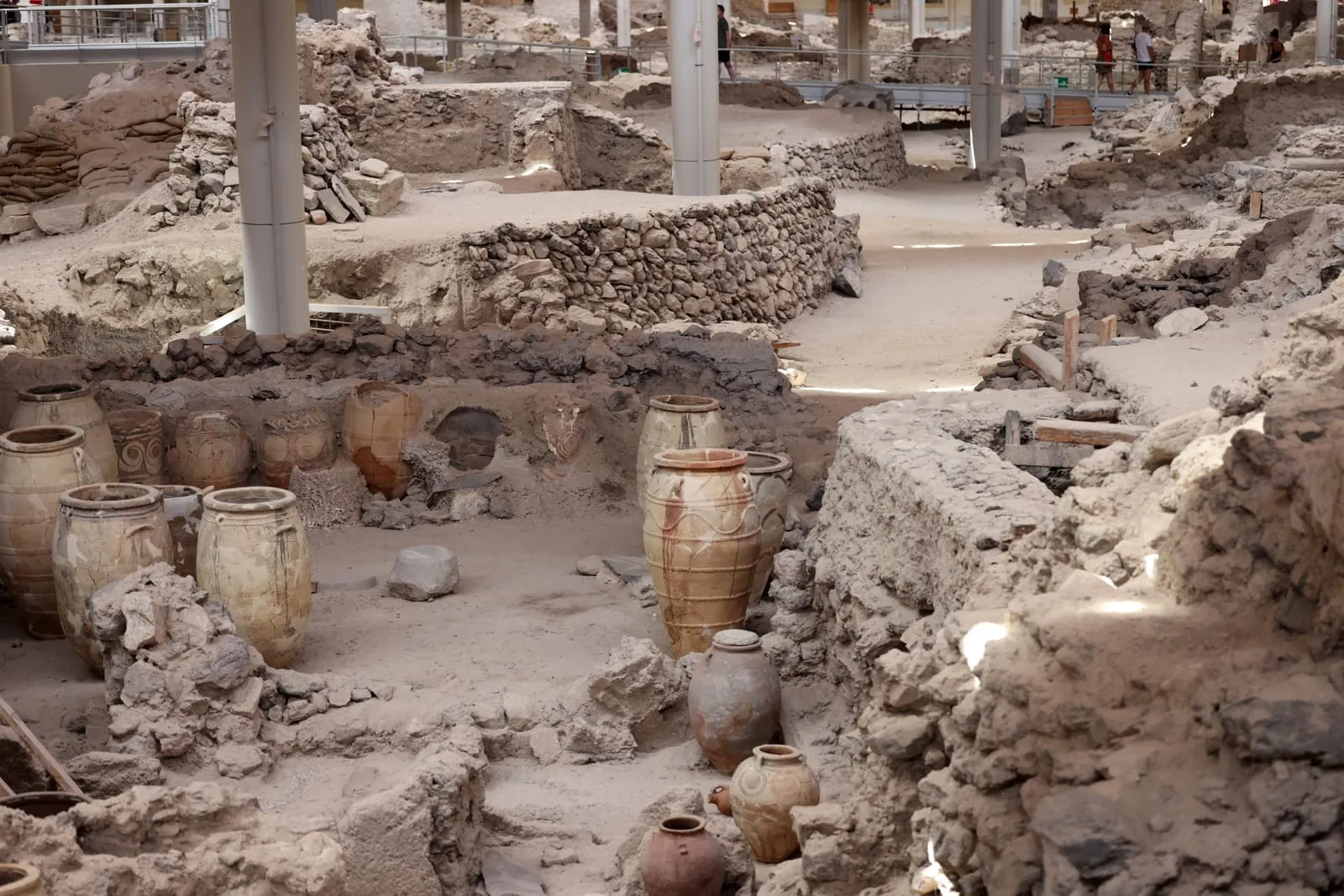 Rows of large clay jars line the walls of an excavated room in Akrotiri. These vessels likely held oil, grain, or wine, revealing the scale of trade and domestic life in this Bronze Age settlement.
