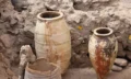 Two large Minoan storage jars stand intact amid the ruins of Akrotiri. The vessel on the right is decorated with circular red and black motifs, while the one on the left appears restored and patched. Their preservation shows how well the volcanic ash sealed the site.