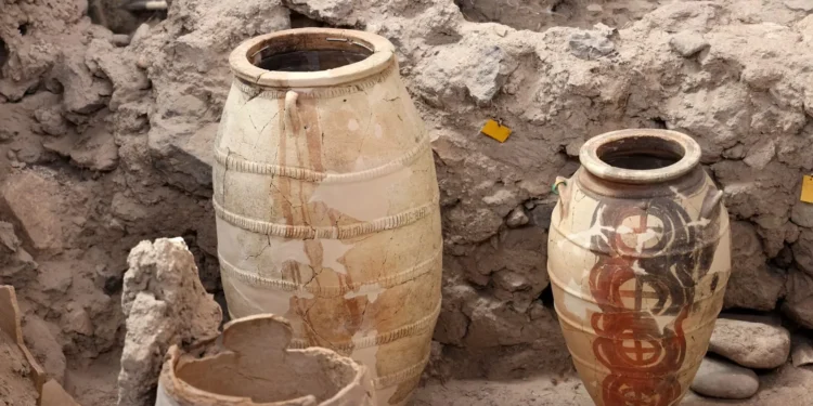 Two large Minoan storage jars stand intact amid the ruins of Akrotiri. The vessel on the right is decorated with circular red and black motifs, while the one on the left appears restored and patched. Their preservation shows how well the volcanic ash sealed the site.