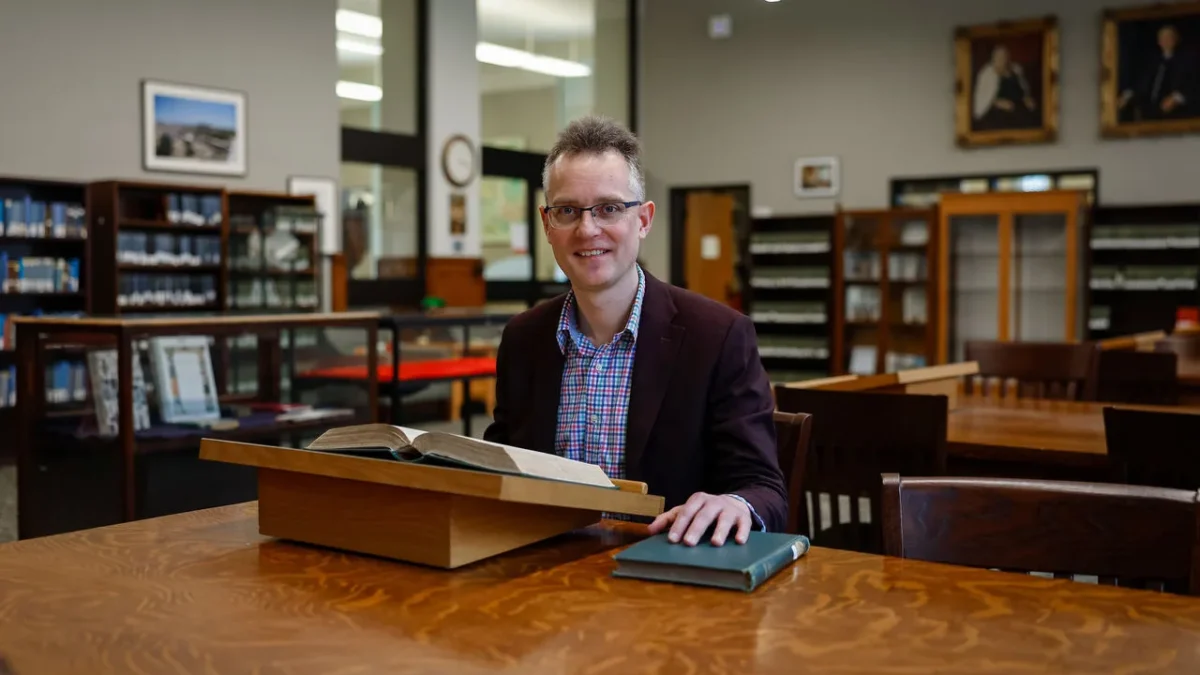 A classicist seated with an open ancient manuscript in a university library