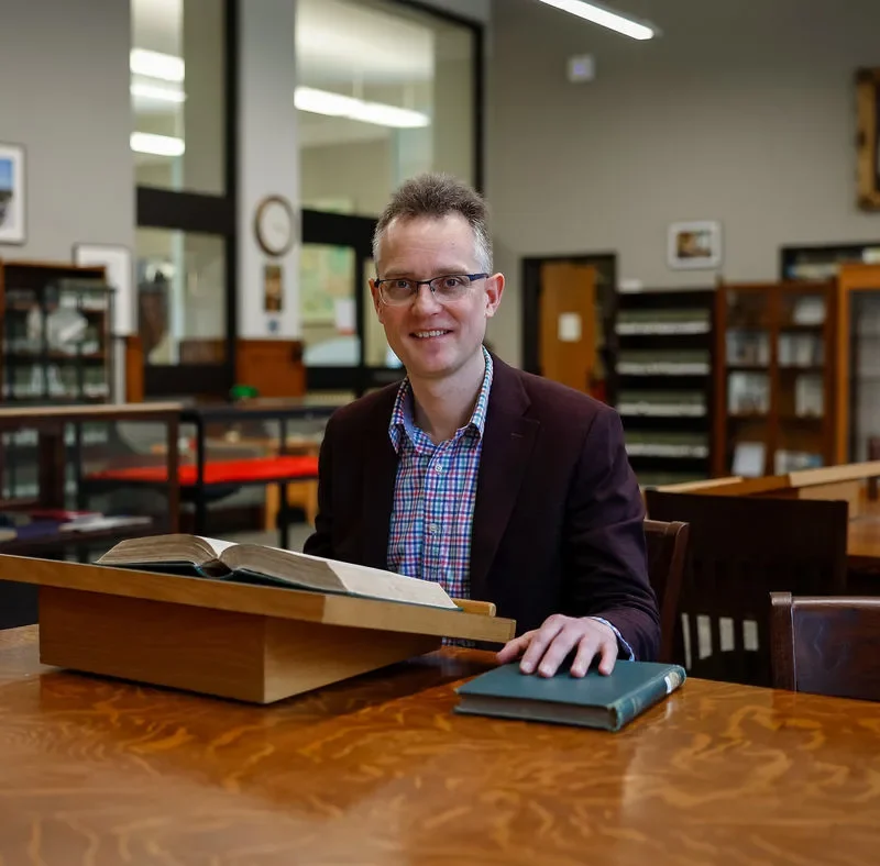 A classicist seated with an open ancient manuscript in a university library