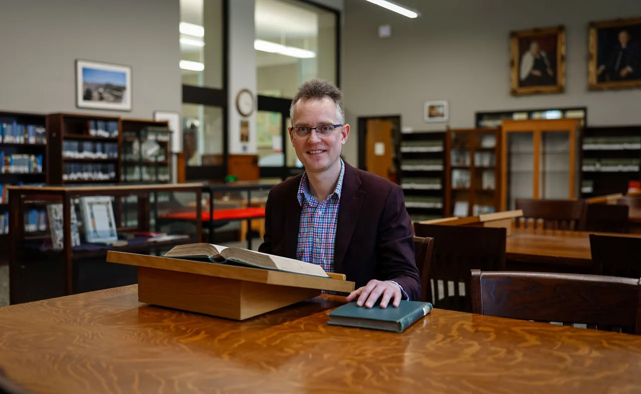 A classicist seated with an open ancient manuscript in a university library