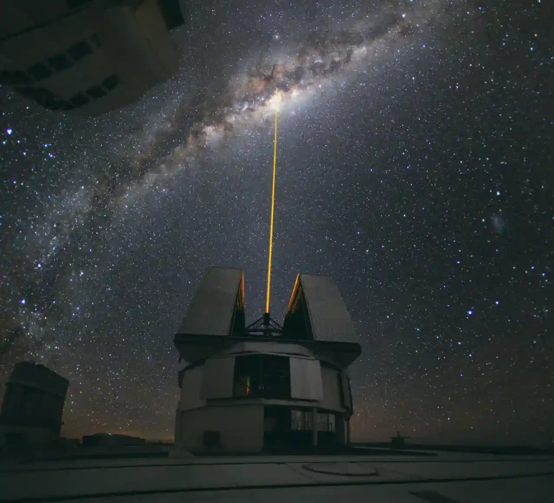A green laser beam aimed toward the center of the Milky Way above an observatory