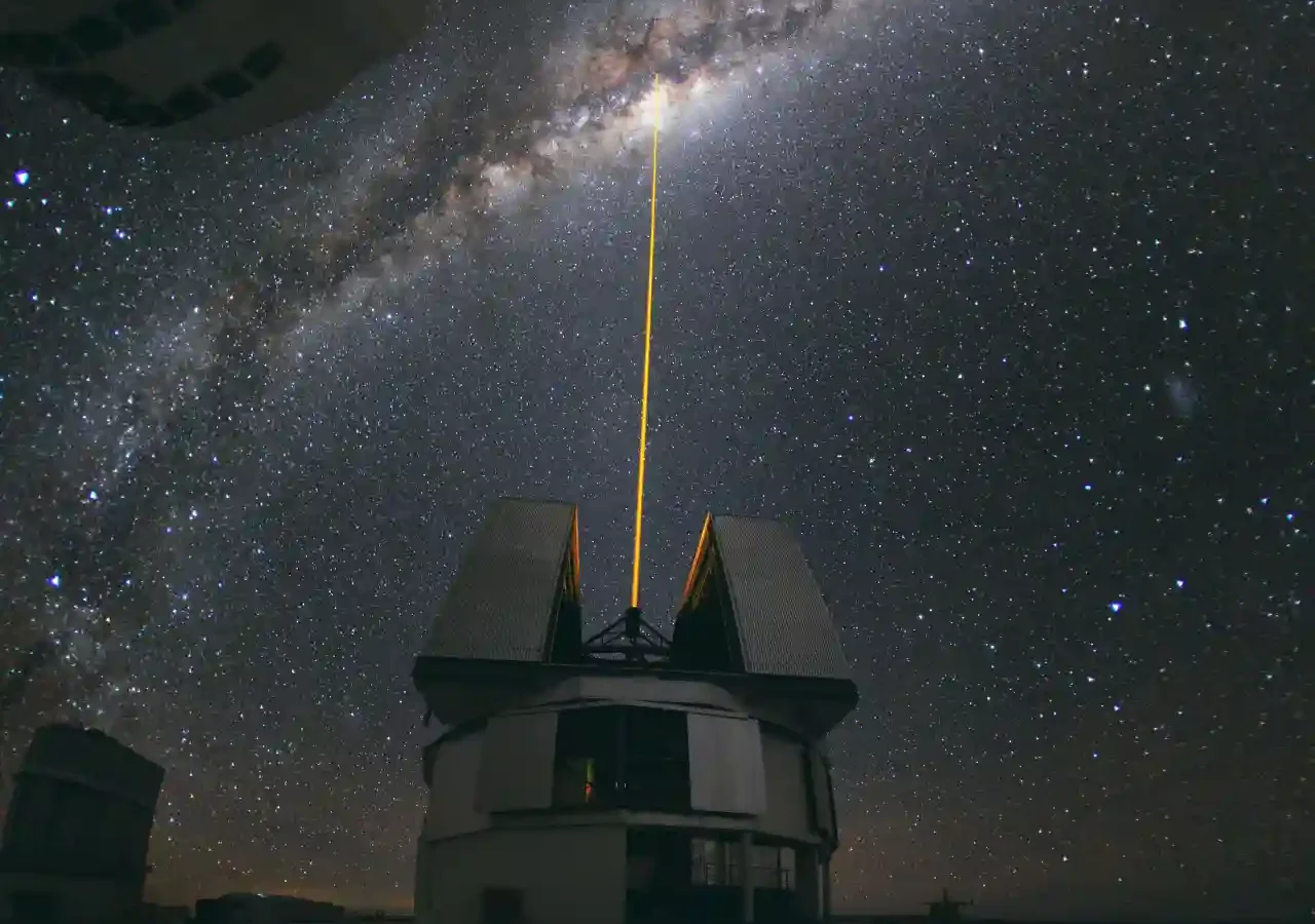 A green laser beam aimed toward the center of the Milky Way above an observatory