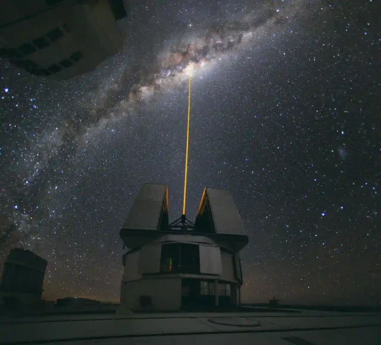 A green laser beam aimed toward the center of the Milky Way above an observatory