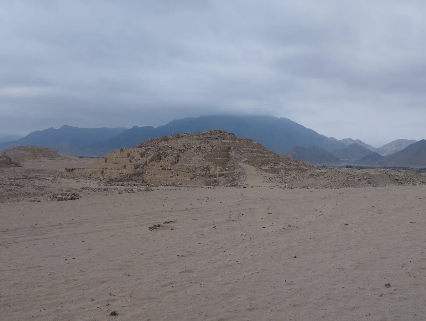 Ancient stepped platform at Caral beneath a cloudy sky