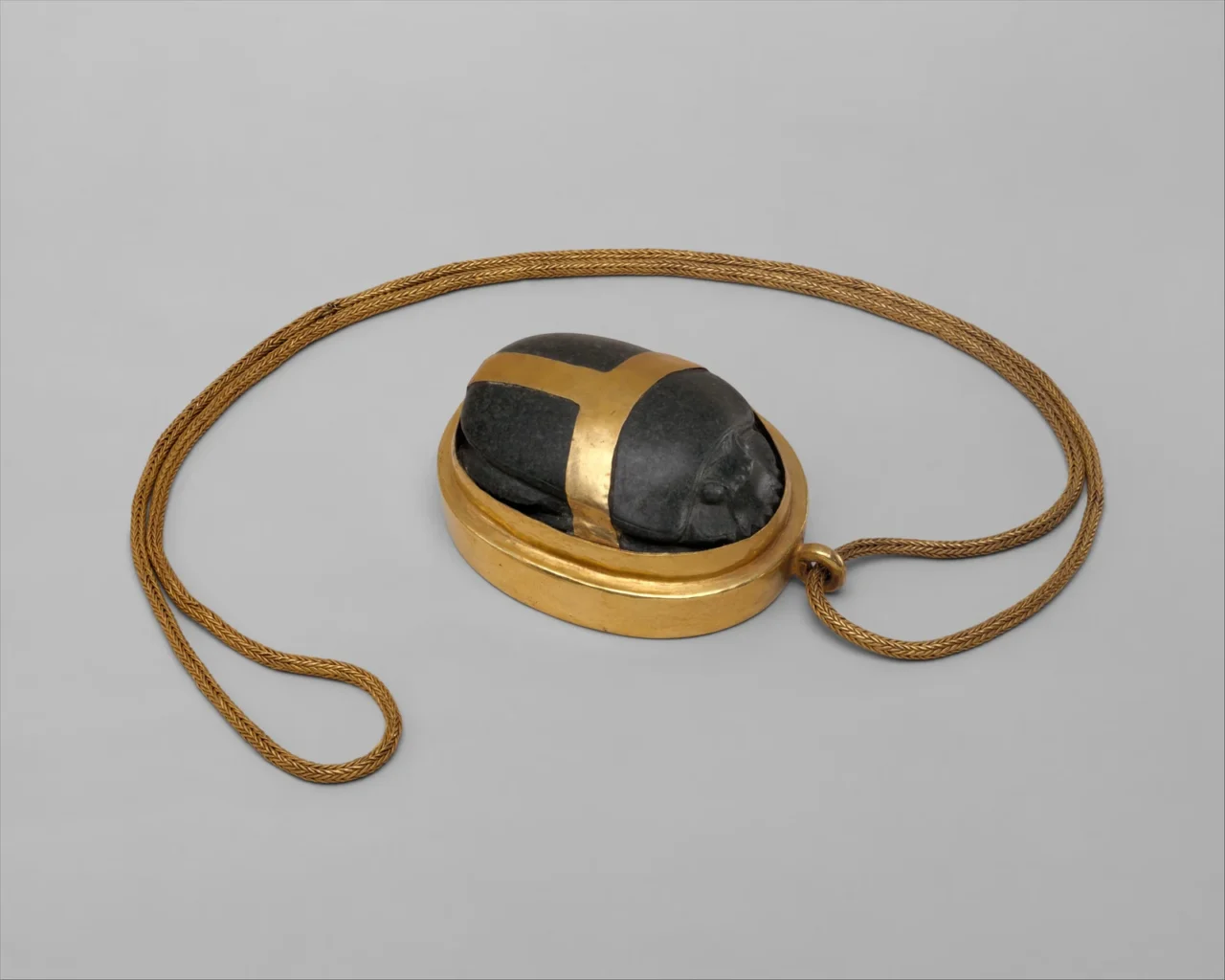Hatnefer’s dark stone heart scarab in a gold mount on a plaited gold chain