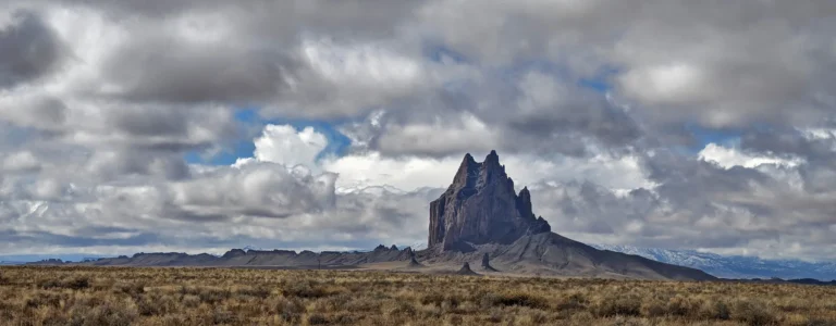 Shiprock’s jagged volcanic peak and exposed rock walls beneath clouds in New Mexico.